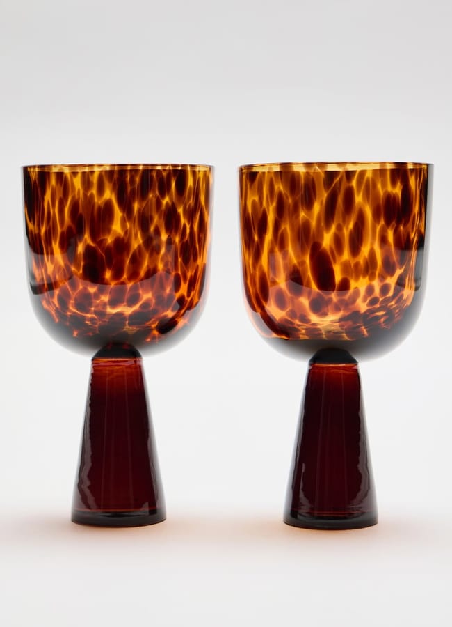 Two stemmed wine glasses with dark amber tortoiseshell-patterned bowls and solid dark brown tapered bases, perfect for autumn tablescape ideas.