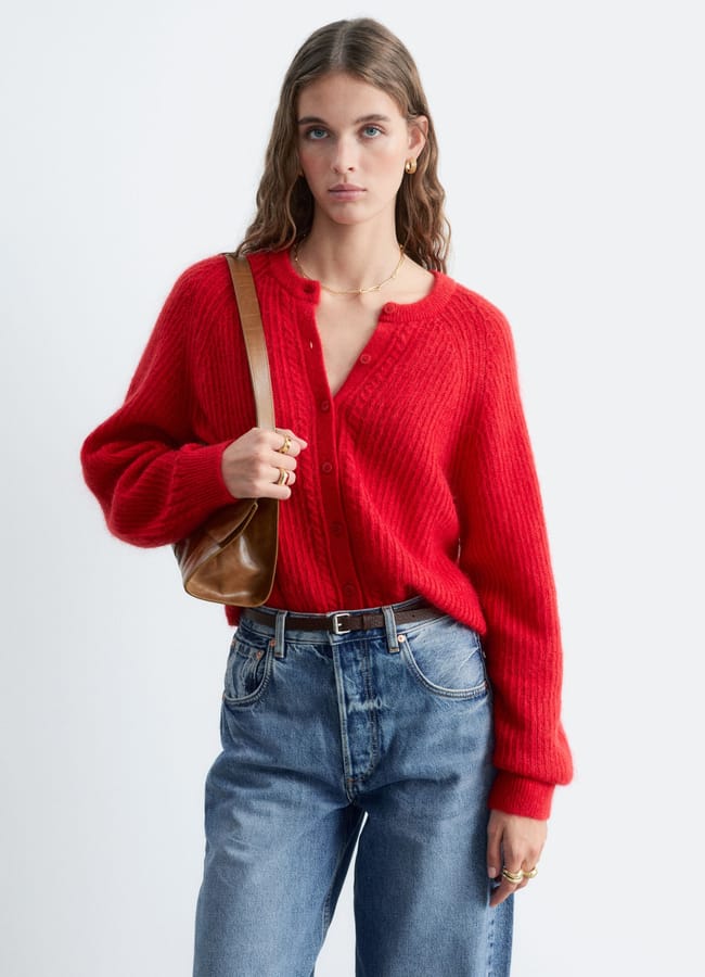 Woman wearing a bright red button-up cardigan and blue jeans, carrying a brown leather shoulder bag.