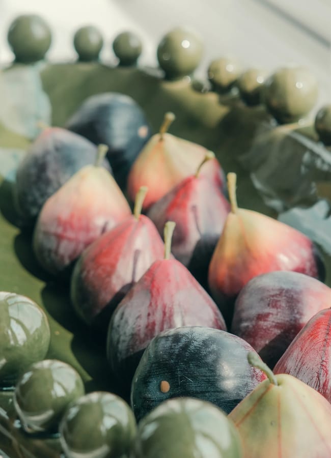 Fresh figs arranged in a long, green ceramic dish with a decorative beaded rim, perfect for autumn tablescape ideas.