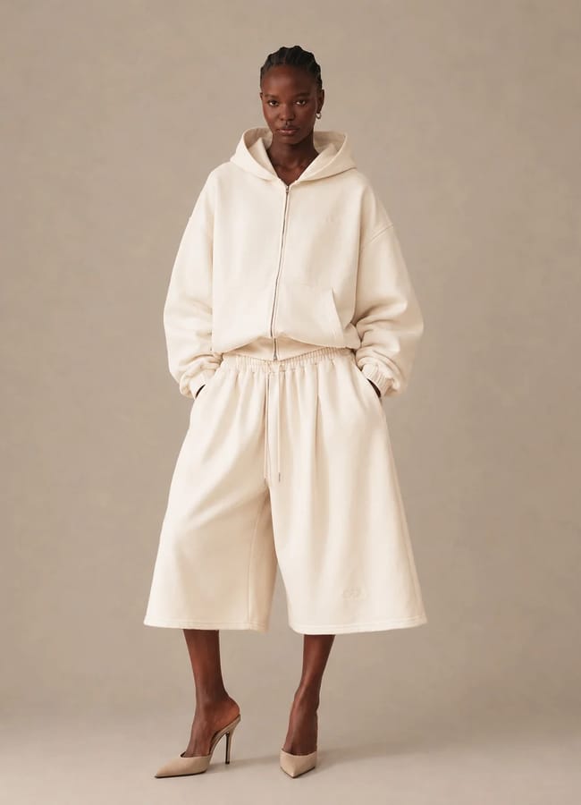 A model wears a matching cream-coloured zip-up hoodie and knee-length wide-leg shorts from a black-owned fashion brand, styled with pointed-toe heels.