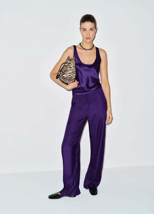 A woman wearing a purple satin vest top and matching drawstring trousers, carrying a zebra-print handbag.
