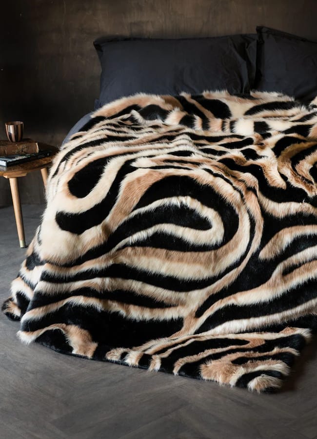 A Rockett St George bed covered with a faux fur throw featuring a tan, black, and white swirling zebra-like pattern.