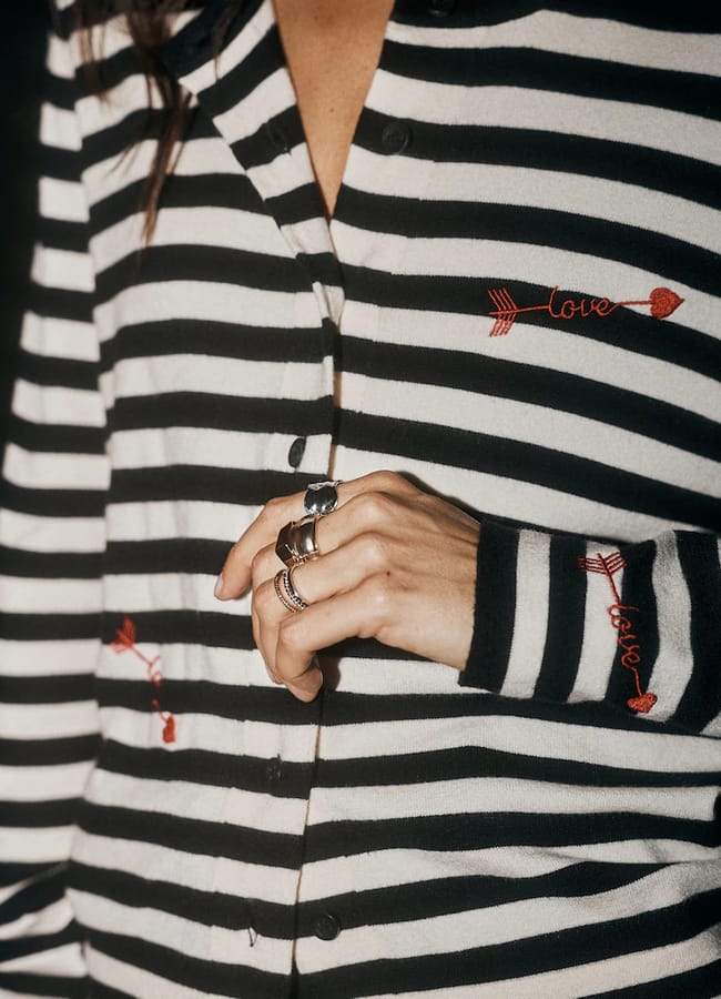 A Rockett St George button-through cardigan with black and white horizontal stripes, featuring red embroidered arrow and love script details on the chest and sleeve.