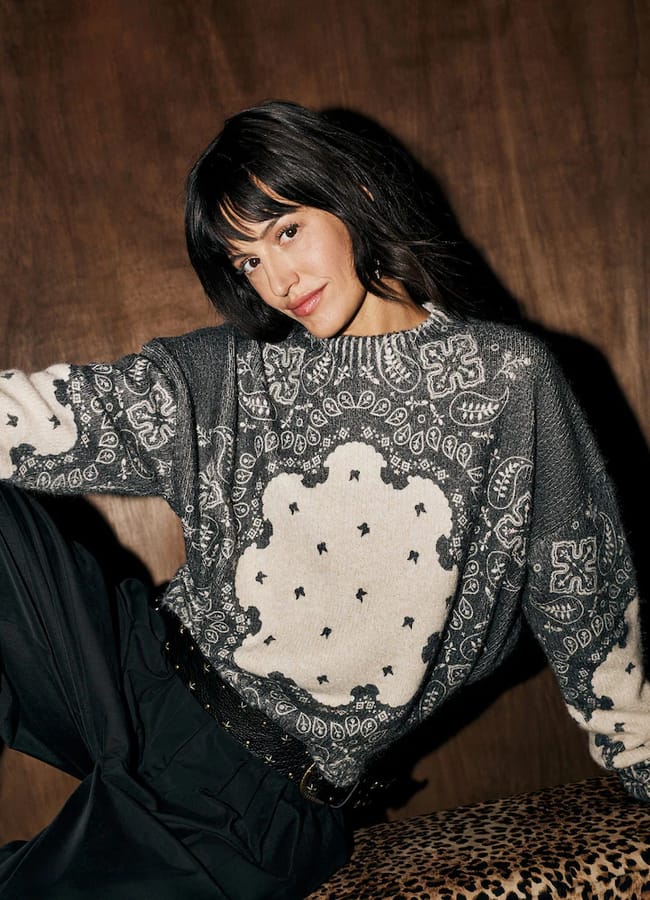 A woman wears a Rockett St George charcoal grey and cream crew neck jumper featuring a bandana-inspired paisley pattern.