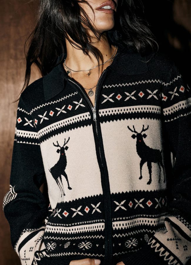 A Rockett St George person wearing a black and cream zip-up jumper featuring a Fair Isle pattern with reindeer motifs.