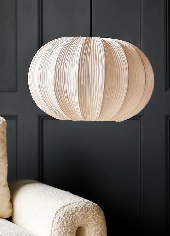 A round, pleated Rockett St George pendant light fitting hanging against a dark panelled wall.