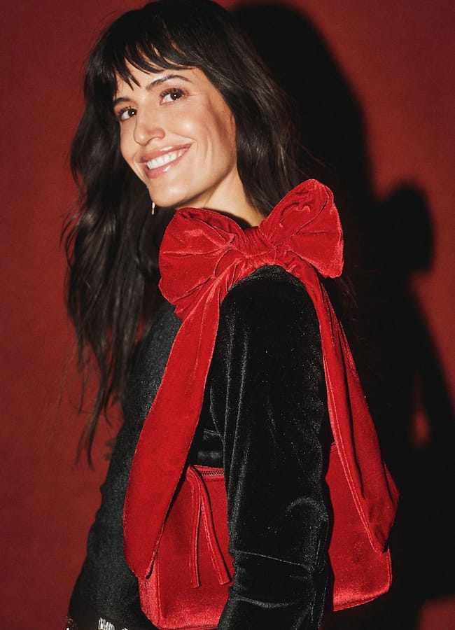 A smiling woman wears a Rockett St George black top accented with a large red velvet bow on the shoulder.