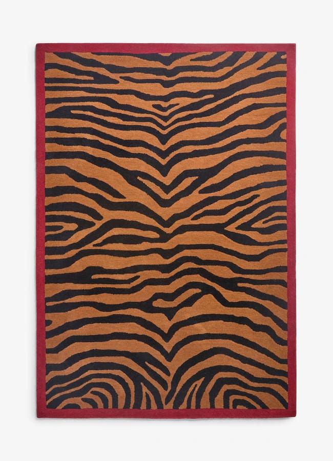 Rectangular Rockett St George rug with a brown and black tiger-stripe pattern and a solid red border.