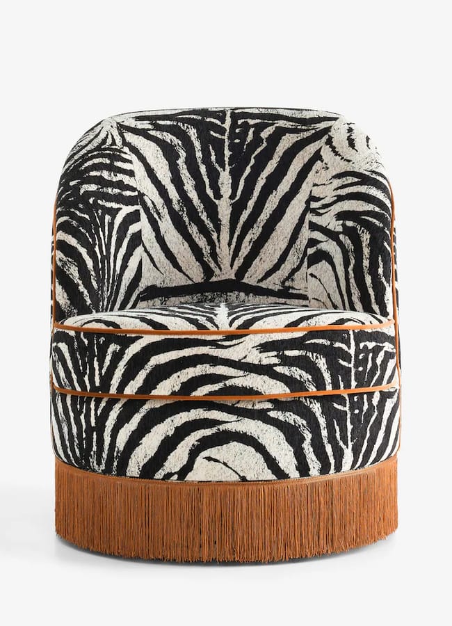 Rockett St George barrel-back accent chair upholstered in black and white zebra print fabric, featuring brown piping and a brown fringe base.