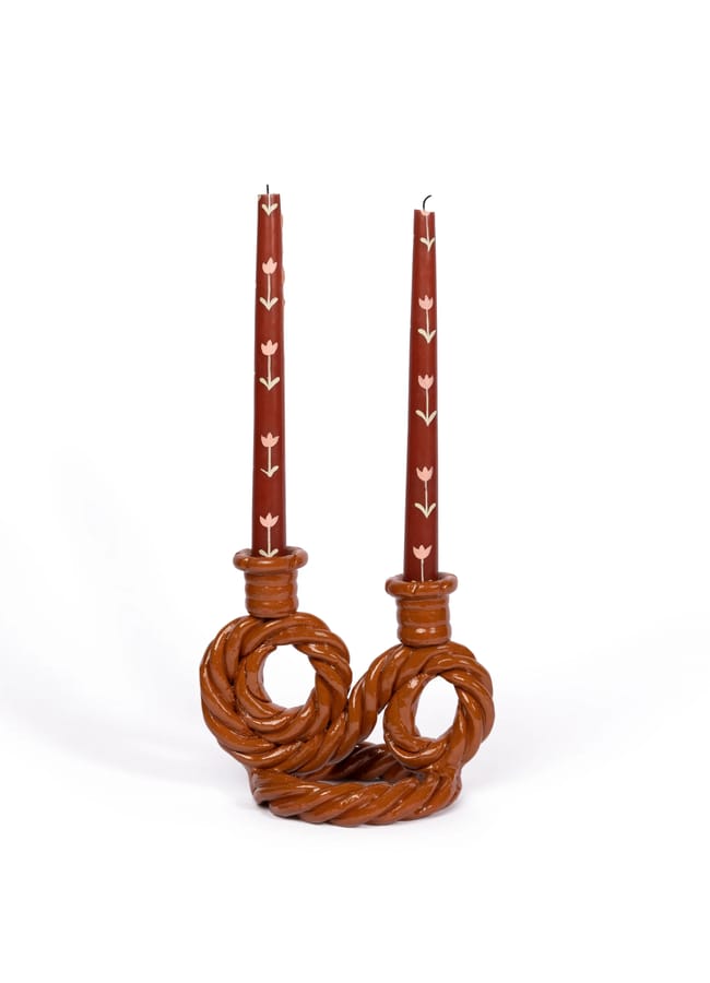 Two red taper candles with white tulip motifs in a twisted, brown ceramic double candle holder, perfect for autumn tablescape ideas.