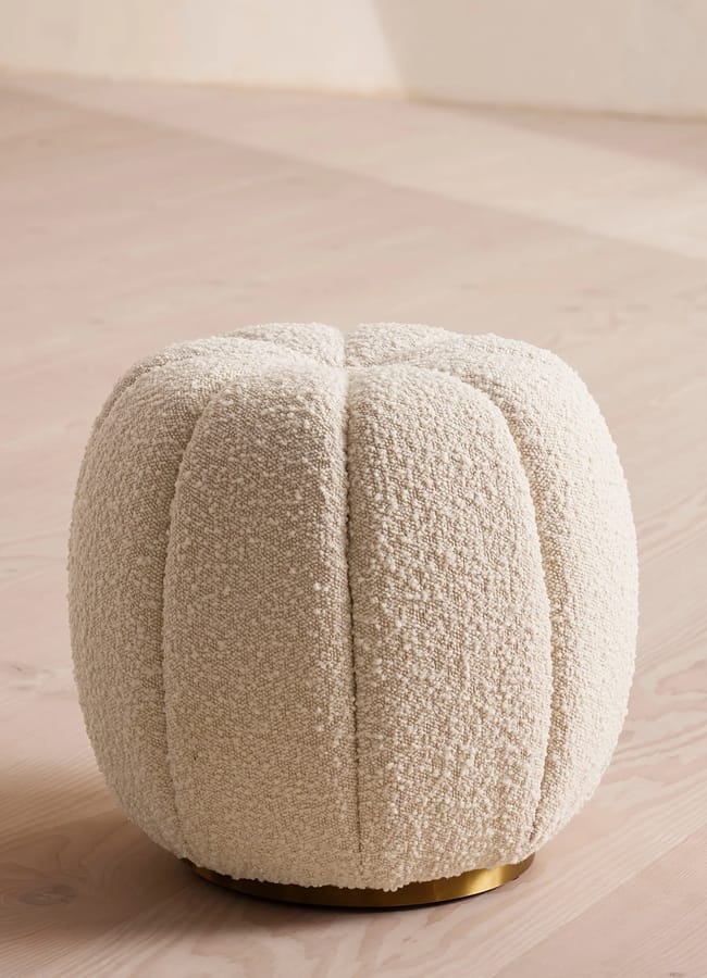 Round cream-coloured bouclé ottoman with a gold base.