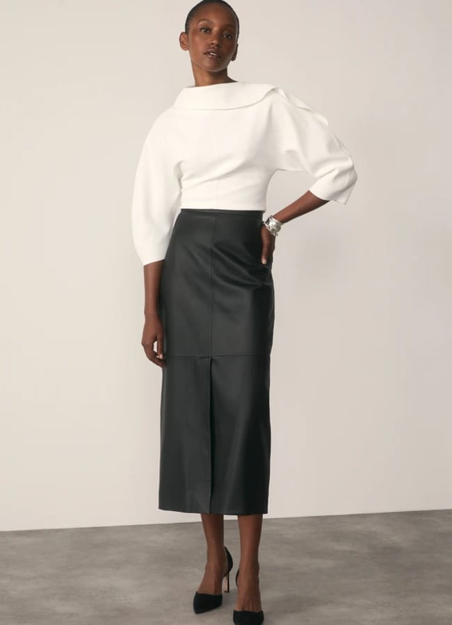 A model wearing a white top with a wide collar and three-quarter sleeves, paired with a black midi-length pencil skirt with a front slit and black court shoes.