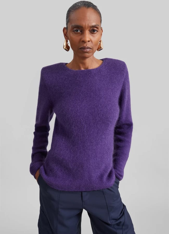 A person wearing a purple crew-neck jumper and dark trousers.