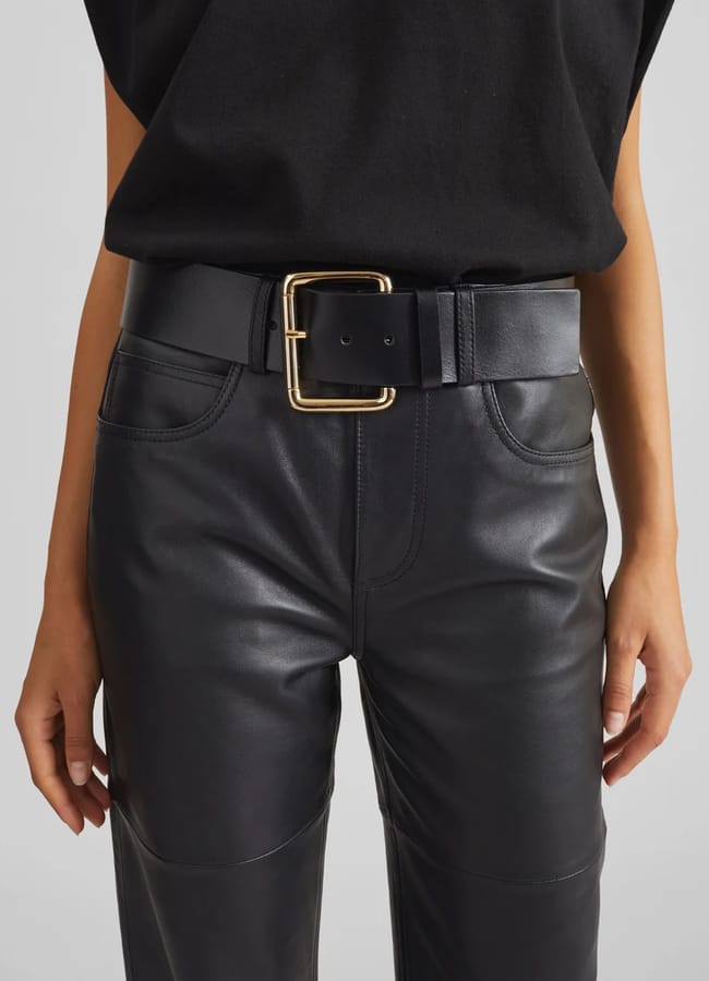 Person wearing black trousers and a black belt with a large gold-tone rectangular buckle.