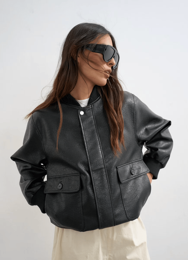 A woman wearing one of the best women's leather jackets in a black bomber style with flap pockets and oversized sunglasses.