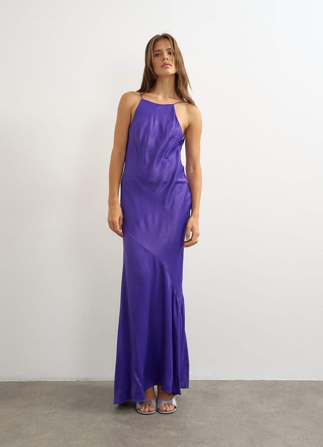 A woman wearing a floor-length, purple, sleeveless satin dress and silver sandals.