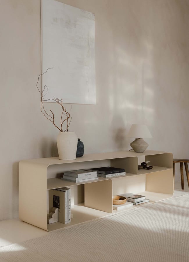 A low, rounded beige shelving unit styled with books, decorative vases, a small lamp, and a wooden bowl, perfect for listening room interior ideas.