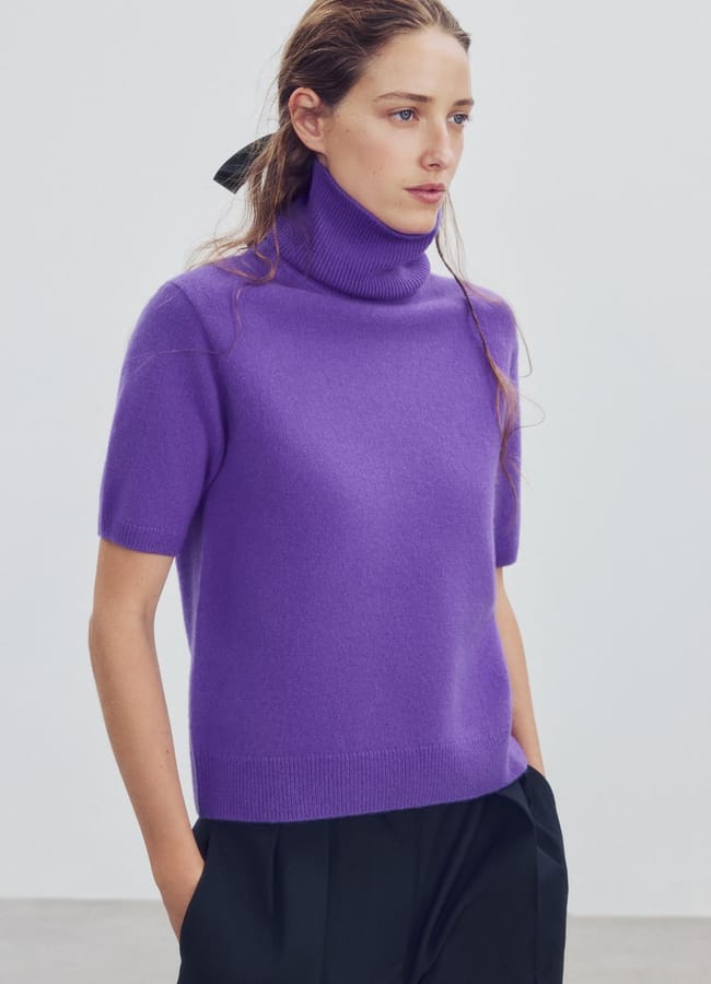 A woman wearing a short-sleeved polo-neck jumper in bright purple.