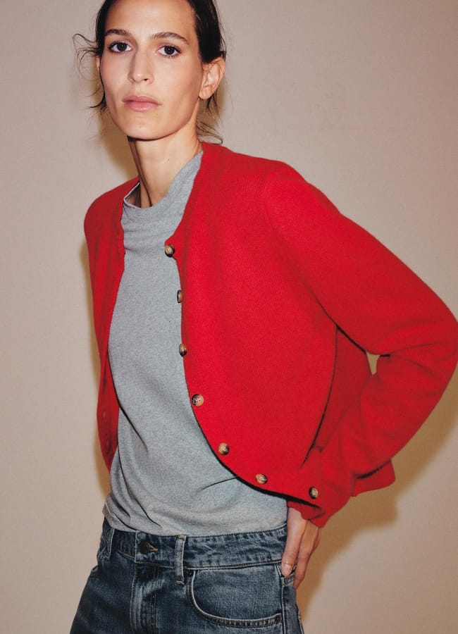 A woman wearing a bright red button-up cardigan over a grey T-shirt and blue jeans.