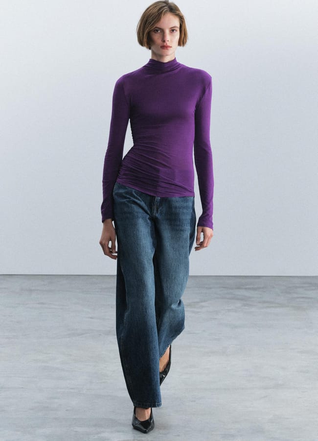 A person wearing a long-sleeved purple polo-neck top and wide-leg blue jeans.
