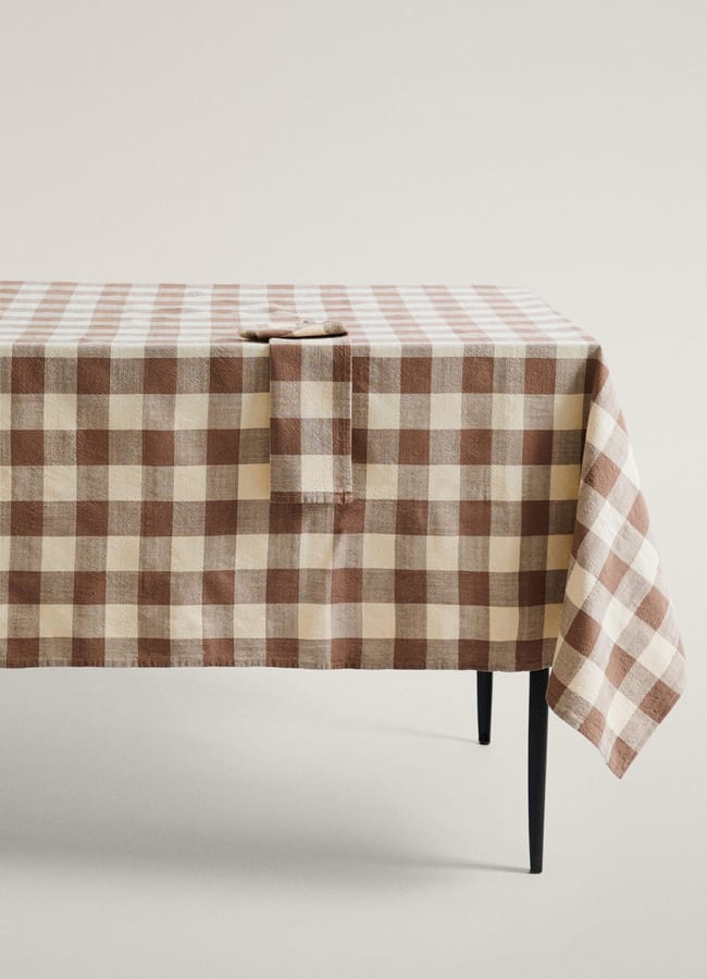 A brown and beige chequered tablecloth draped over a table with a matching folded serviette on top, perfect for autumn tablescape ideas.
