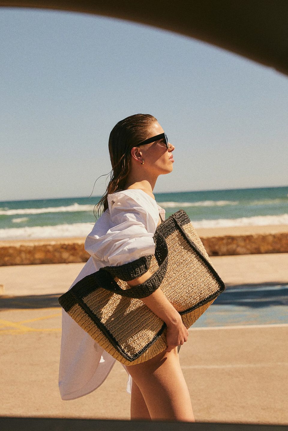 model on beach holding large raffia tote